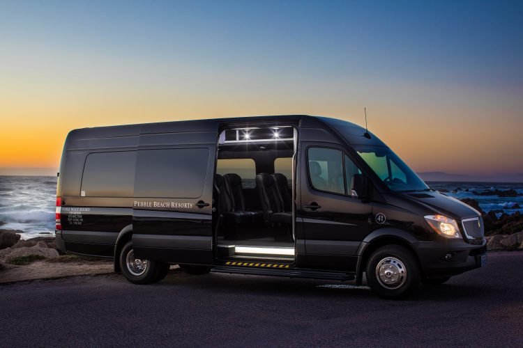 A black shuttle van parked by the ocean at sunset