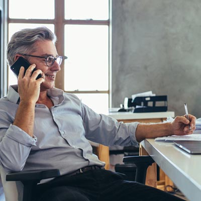 A man at his desk on the phone writing on a paper
